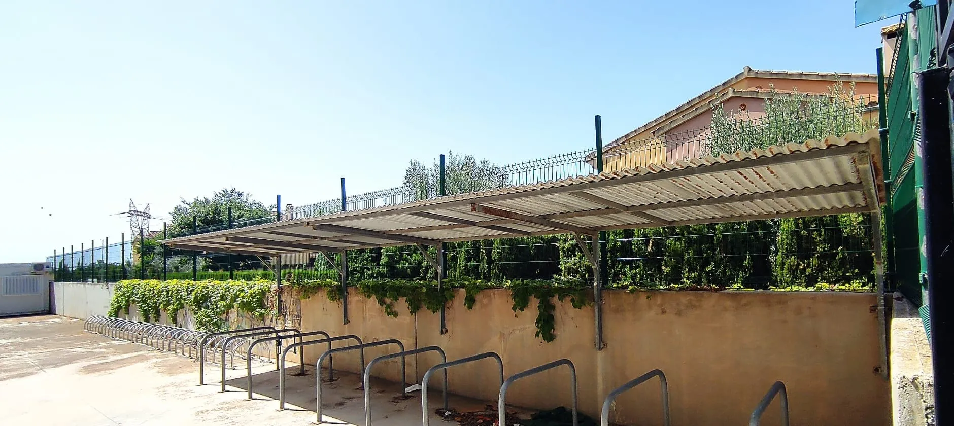 Row of steel bike racks under a canopy next to a wall