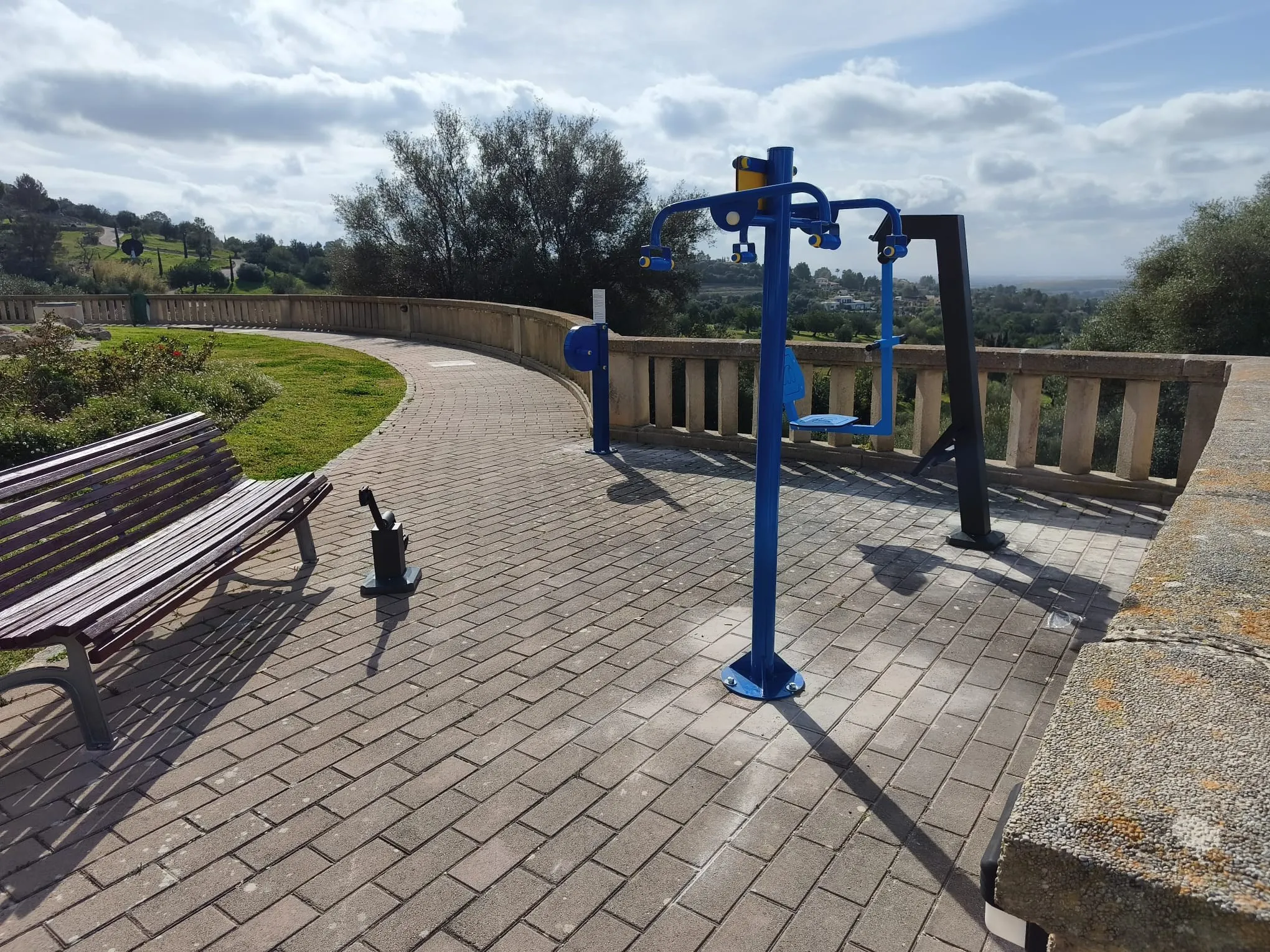 Aparatos de gimnasia biosaludable instalados en un paseo con barandilla de piedra