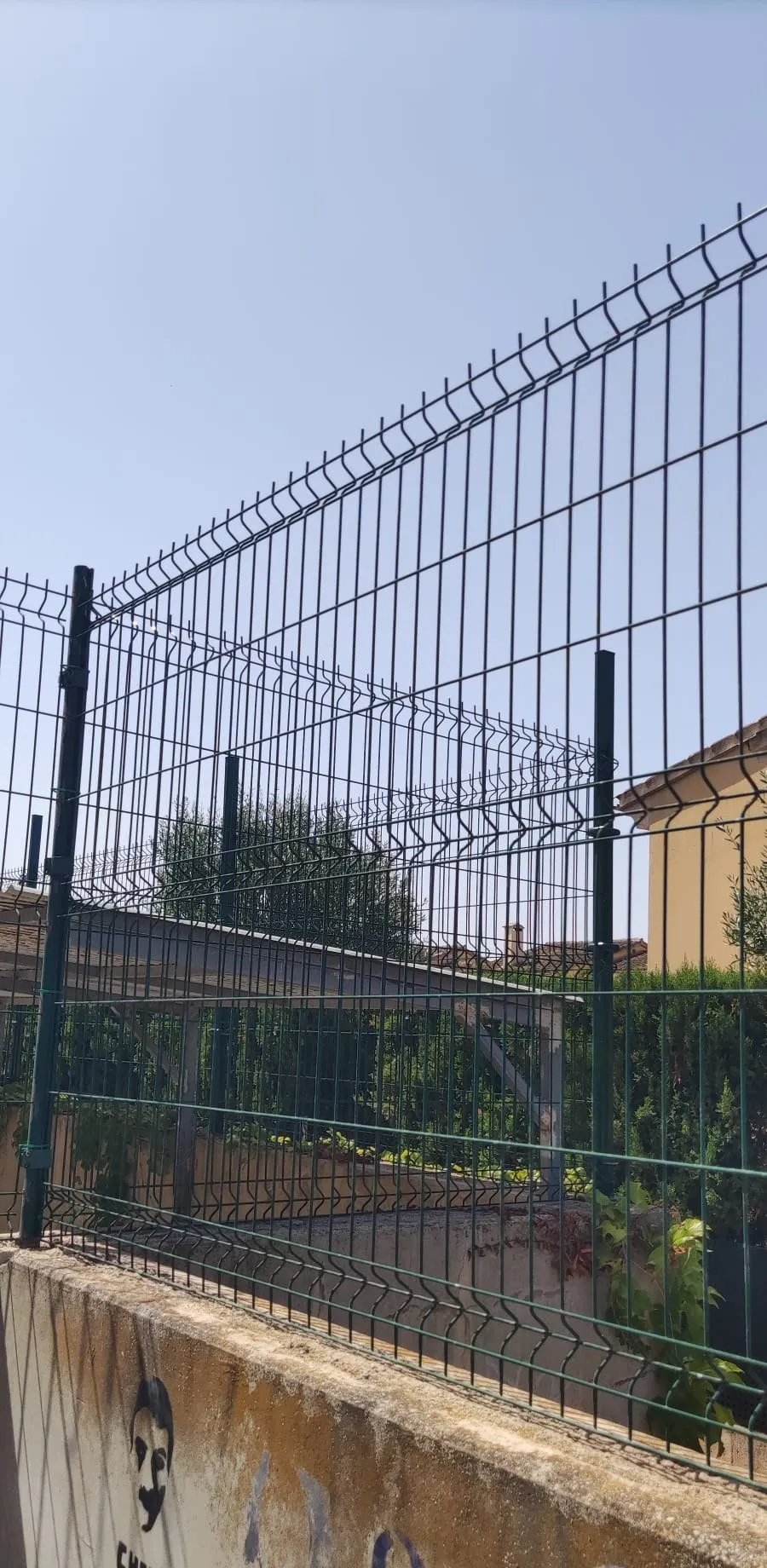 Cerramiento de malla metálica verde recién instalado sobre murete