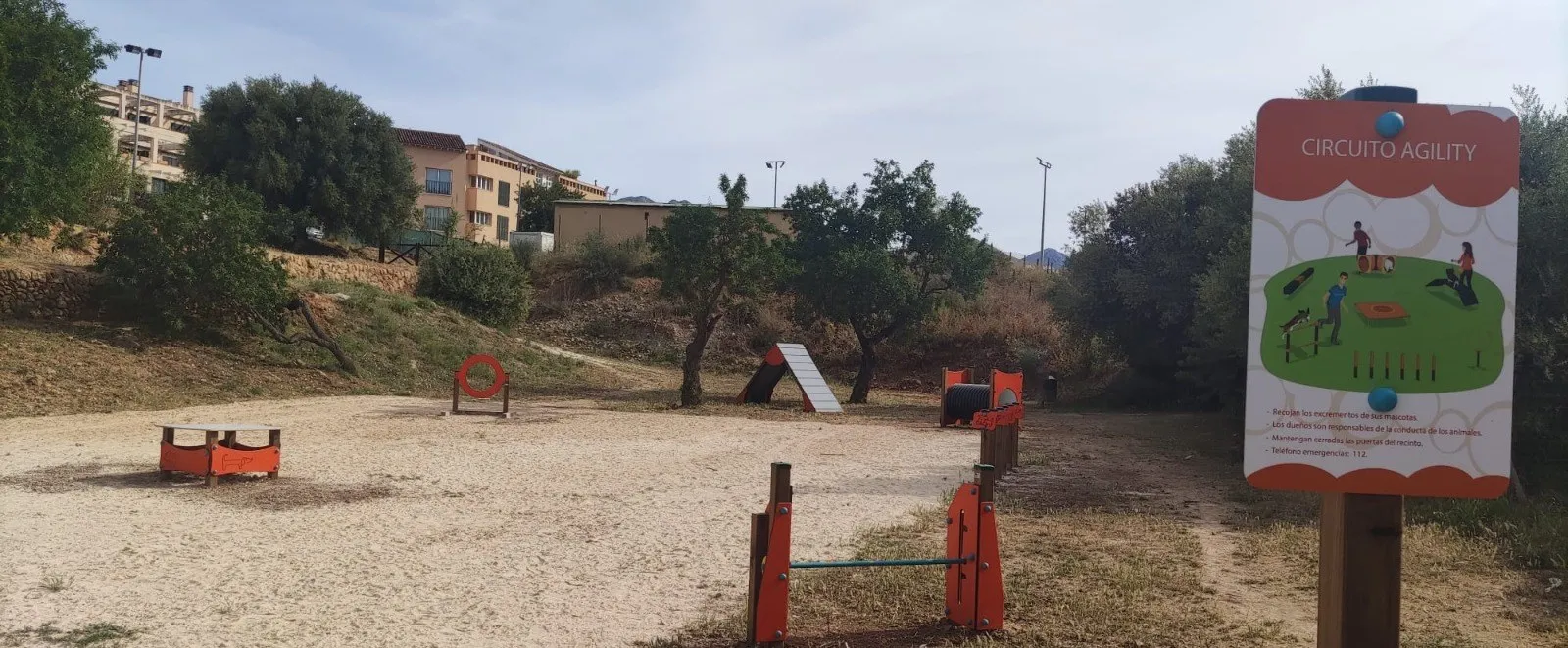 Circuito Agility en área natural con cartel informativo, aro, empalizada, túnel y vallas de salto