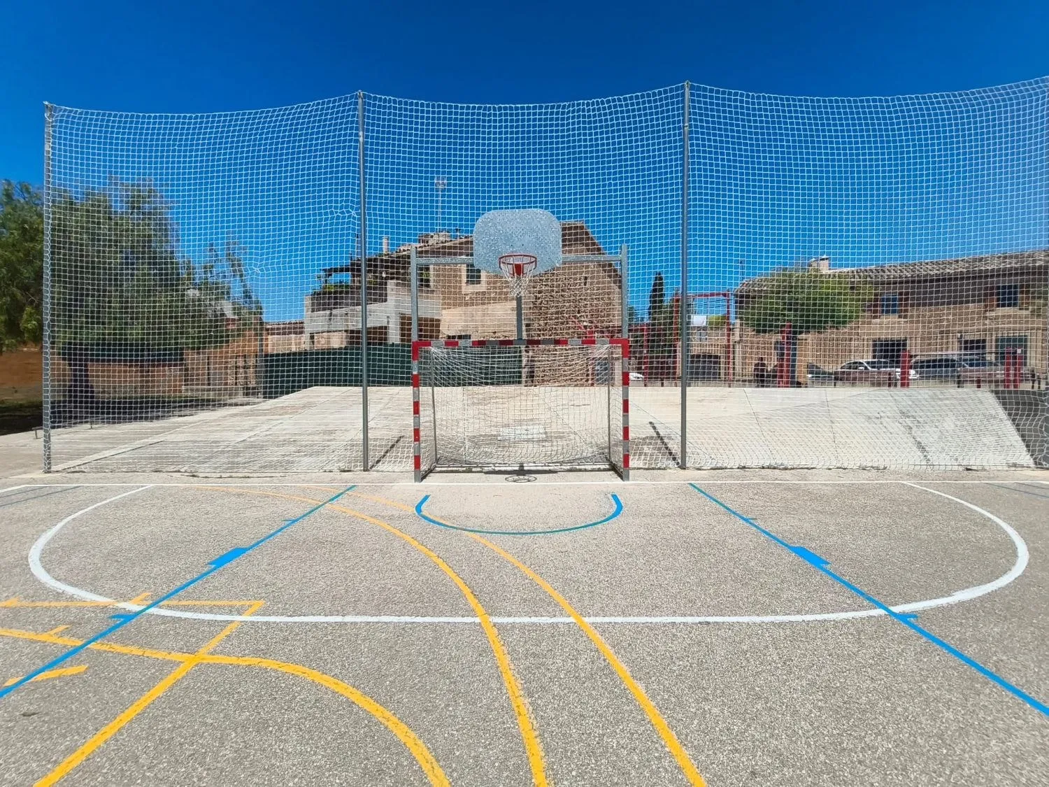 Goal and basket on a multi-sport court with lines for several sports and safety netting