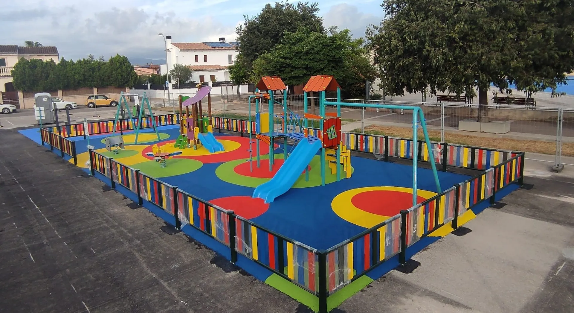 Parque infantil terminado con pavimento de caucho de círculos de colores y vallado multicolor