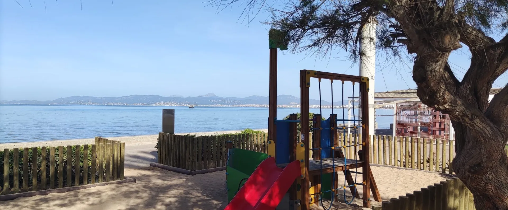 Estructura de juego con tobogán y red de trepa sobre arena frente a la bahía