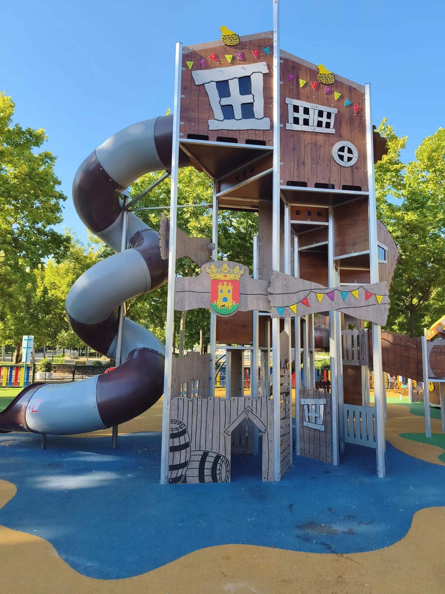Themed wooden play tower with a spiral tube slide on blue rubber surfacing