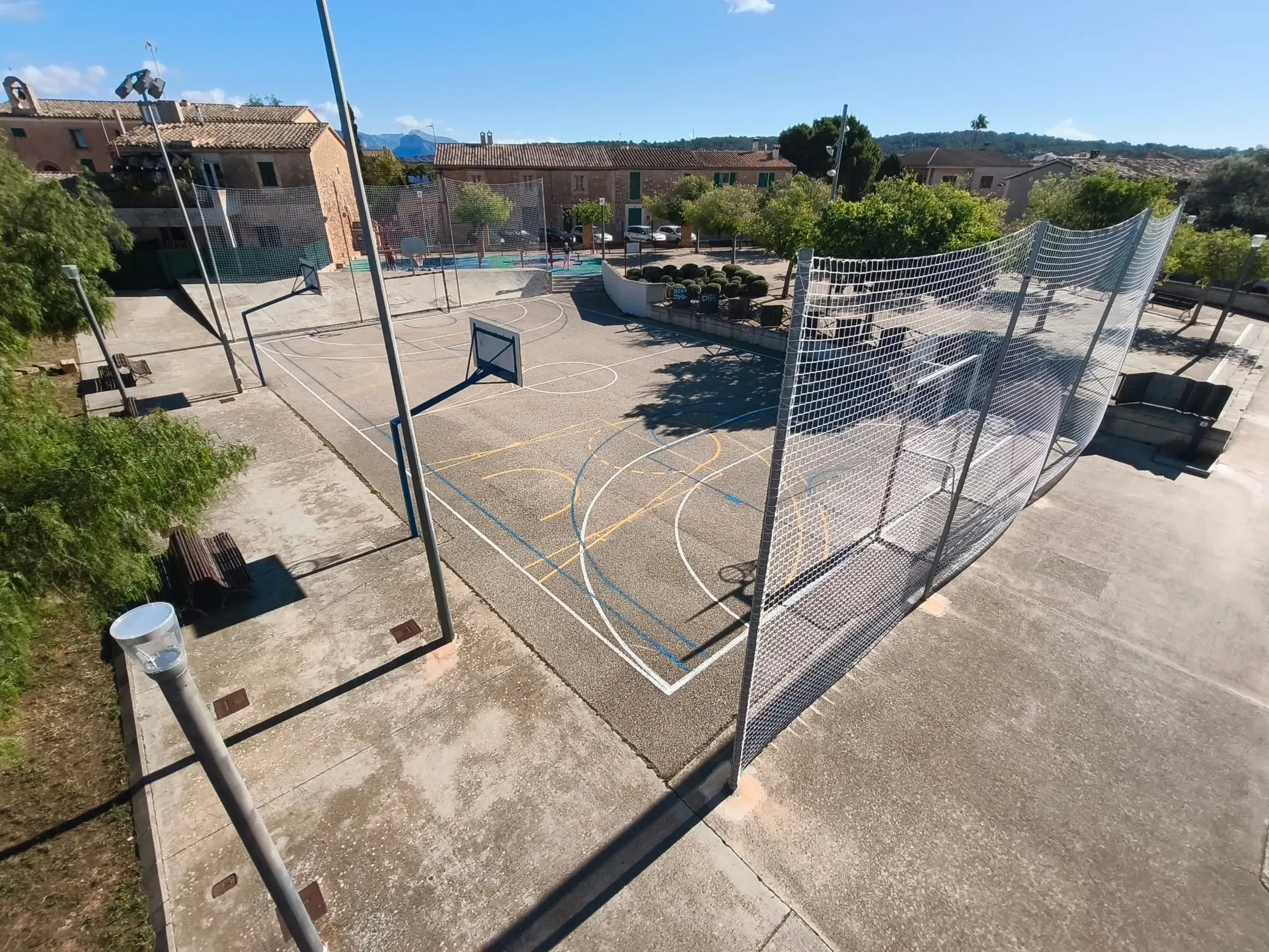 Vista elevada de una pista multideporte con red parapelotas y porterías