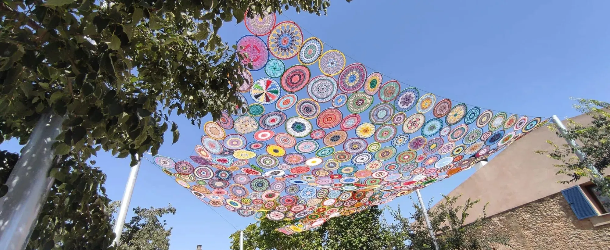 Shade canopy made of colourful crochet mandalas stretched over a street