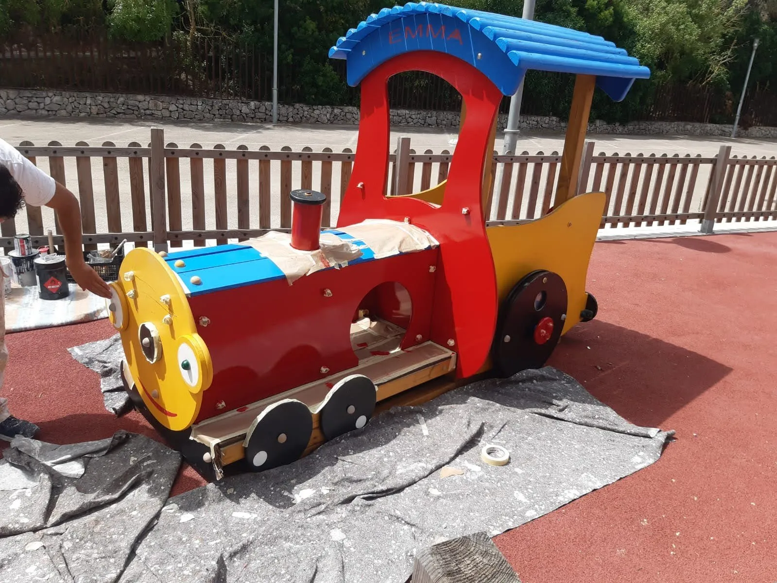 Operario restaurando y pintando un tren de madera de un parque infantil